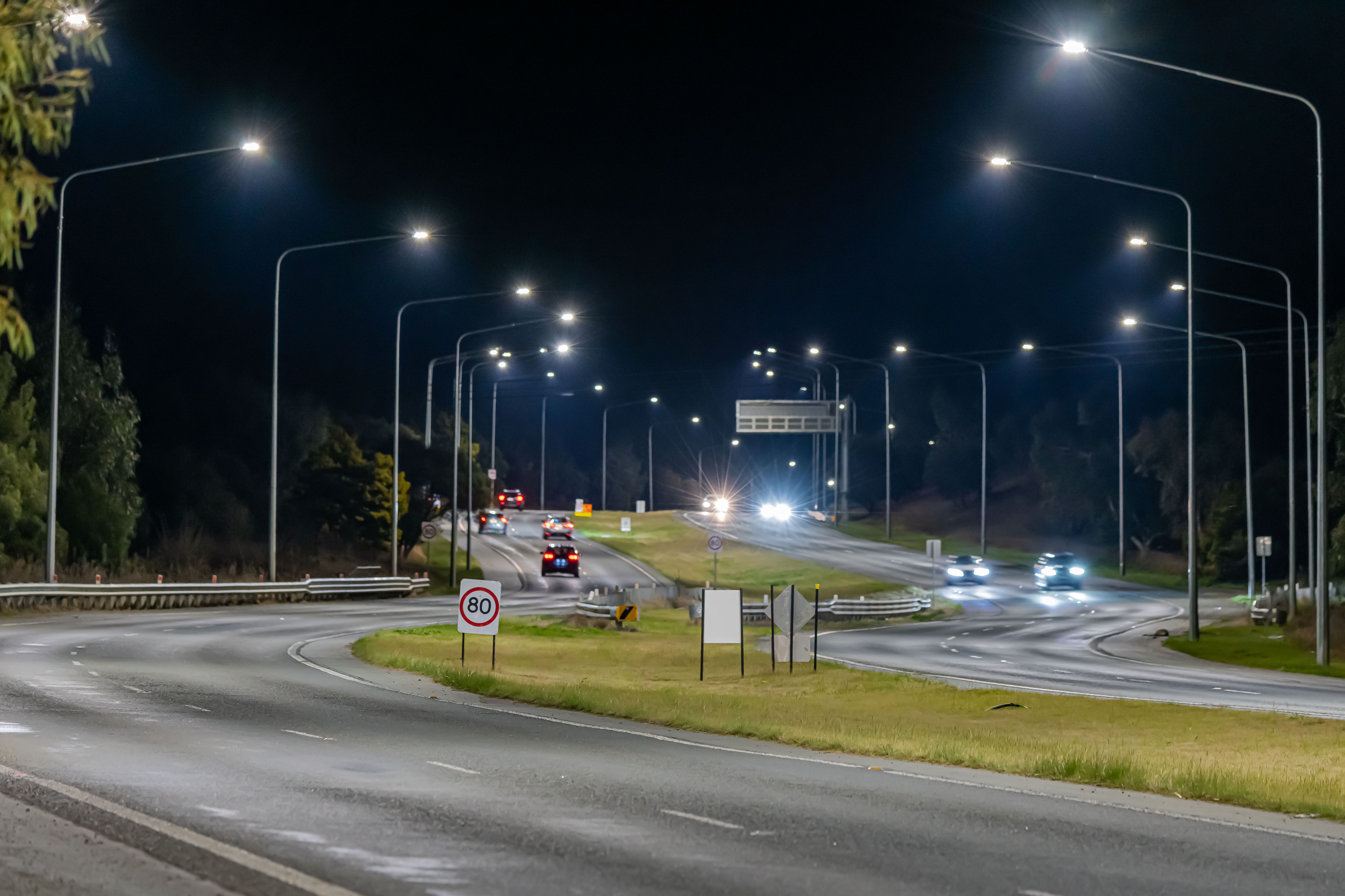 A curvy section of road with street lights on either side. The cars are blurred into neon ribbons of light.